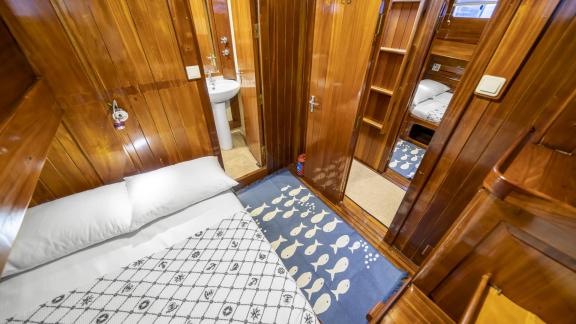 The cabin features a bed with a patterned cover, a blue rug, and direct access to the bathroom.