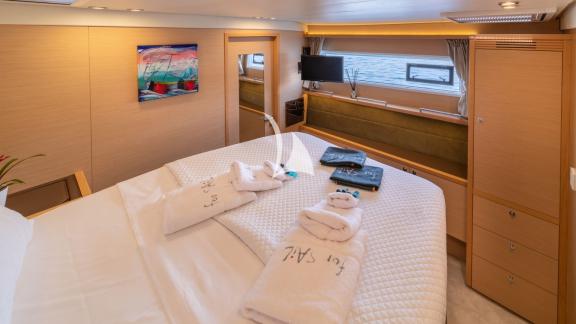 Luxurious cabin with double bed, For Sail towels, flat-screen TV, and warm wood tones.