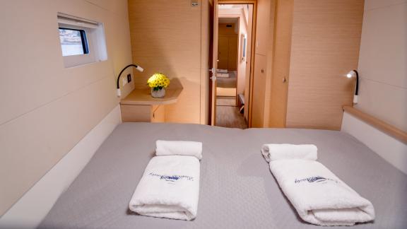 Comfortable cabin with a large bed, desk, and side window on a catamaran, with a view into the hallway.