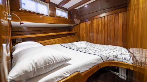 The cabin features a double bed with a patterned cover, wooden walls, and two windows for natural light.