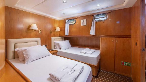 A cosy twin cabin on a Bodrum gulet, equipped with two single beds, wood panelling and soft lighting.