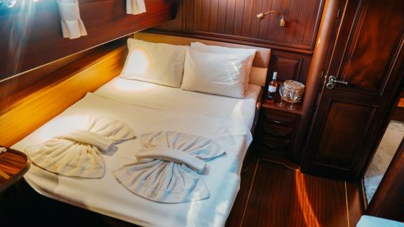 A cosy bedroom on a sailing ship with a comfortable double bed, wood panelling and natural light.