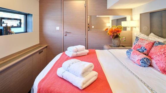 Elegant cabin on the catamaran with a double bed, decorative pillows, coral blanket, and fresh towels.