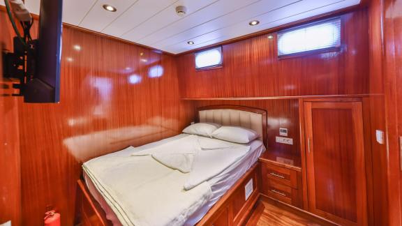 A cozy cabin on the Gulet Kasapoglu 6 featuring a double bed, wood paneling, and a TV.