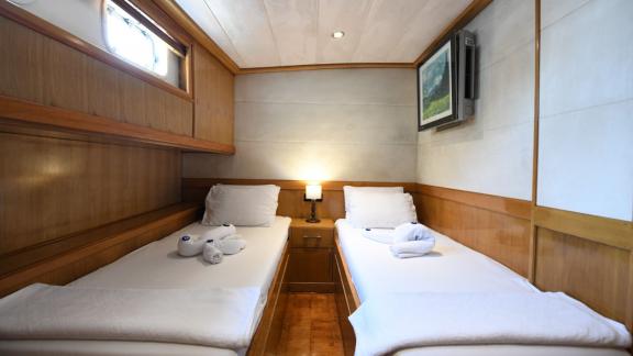 Cabin with two single beds, a porthole, and a painting on Gulet Cemre Mila.