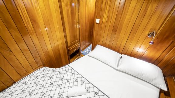 The cabin features a bed with a patterned cover, wooden walls, and a small storage area with a mirror.