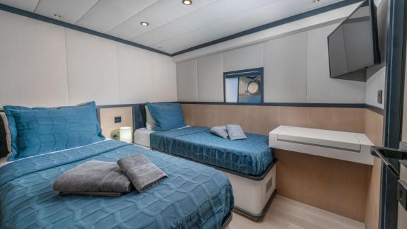 Modern and comfortable cabin room with two single beds, blue bed covers, and wall-mounted TV.
