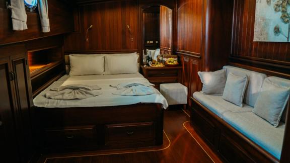 A luxurious ship's cabin with a comfortable double bed, a sofa and elegant wooden furnishings.