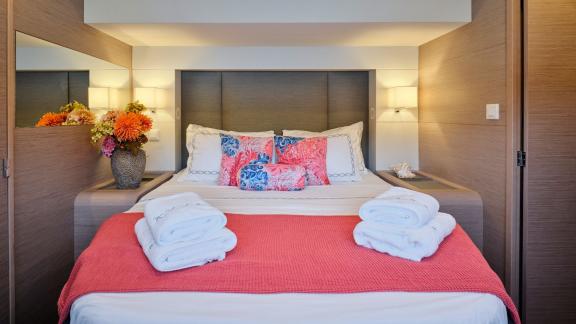 Cabin on the catamaran with a double bed, coral blanket, fresh towels, and a floral arrangement.