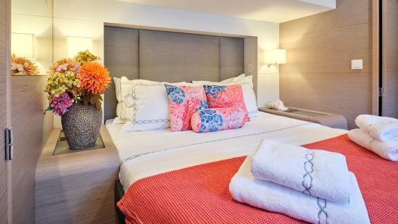 Cozy cabin on the catamaran with a double bed, coral blanket, fresh towels, and a floral arrangement.