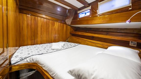 The cabin features a large double bed with a patterned cover, wooden walls, and two windows.