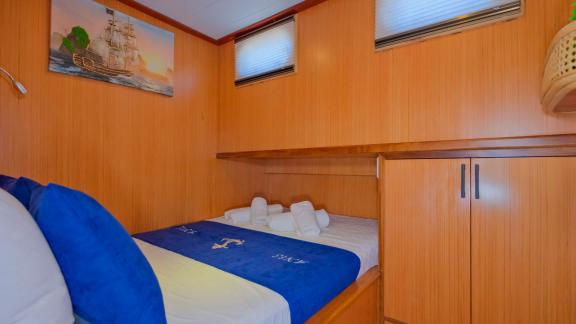 Compact single cabin on Gulet Anes with nautical linens and a decorative ship painting.