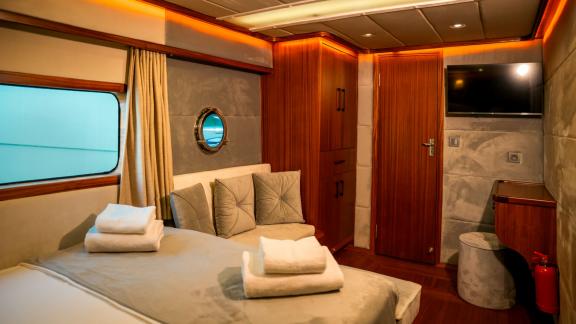 Stylish guest cabin with TV, wood finishes, and a comfortable sitting area on board Oggusto.