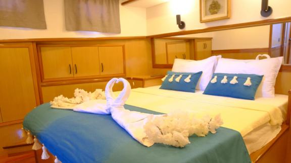 This cabin features a comfortable double bed with blue linens and decorative towel figures, creating a maritime ambiance