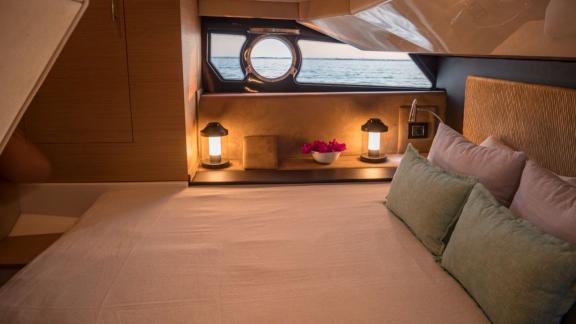 The motor yacht's cabin features a large bed, cushions, and a sea view through the window.