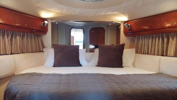 Großes Bett mit dunklen Kissen, cremefarbene Vorhänge und Holzelemente im Raum.