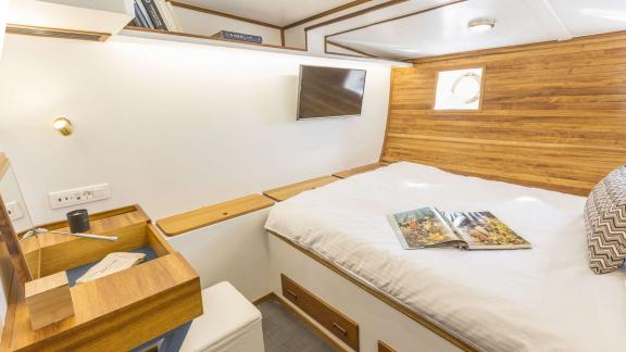 The cabin features a double bed, TV, desk and small porthole windows.