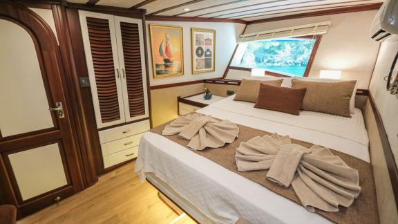 A cosy cabin on the Gulet Tarkan 5 with a large bed, stylish wooden furniture, a window with a sea view and tasteful dec