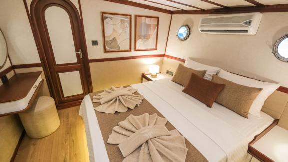 The stylish sleeping cabin of the Gulet Tarkan 5 with a large bed, elegant wooden furniture, decorative cushions and soo