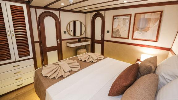 A comfortable cabin on the Gulet Tarkan 5 with a large bed, decorative towels, air conditioning and stylish murals.