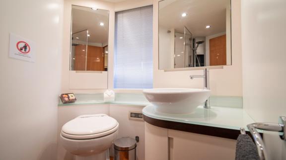 Das Bad verfügt über ein rundes Waschbecken, WC und Duschkabine. Spiegel mit Licht betonen das moderne Design.