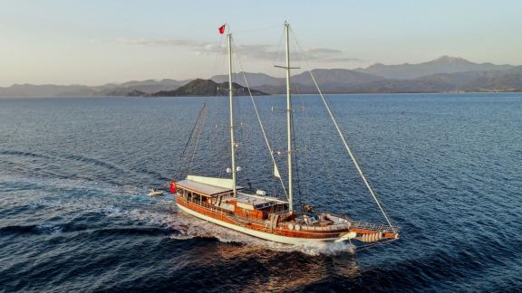 two-masted gulet on a calm sea against a mountain backdrop.