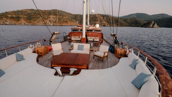 Spacious deck of a yacht with a luxurious wooden seating area and white upholstery, complemented by blue cushions.