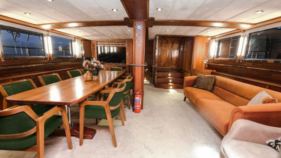 A cosy saloon on a yacht with a dining table, green chairs and a comfortable sofa.