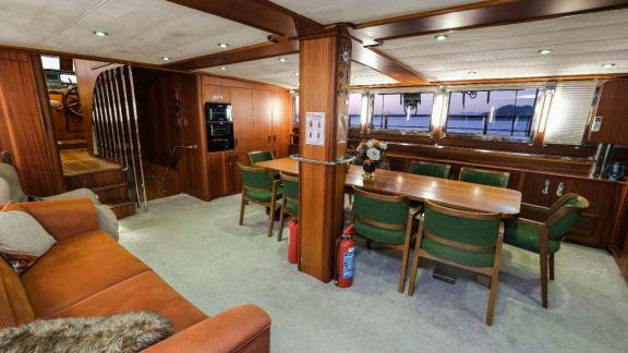 Einen gemütlichen Salon auf einer Yacht mit einem Esstisch, grünen Stühlen und einem bequemen Sofa.