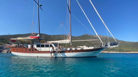 The Gulet Ali Aga 1 anchored in a turquoise bay, surrounded by green hills in Göcek.