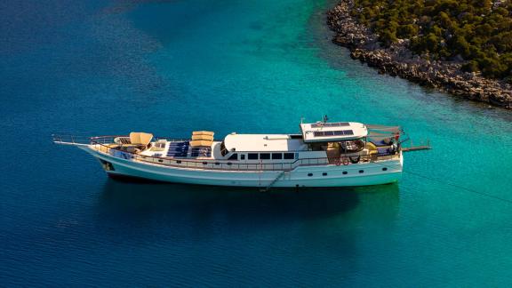 In Göcek gulet charter option Always Smile side view in clear water with sunbeds and spacious deck visible.