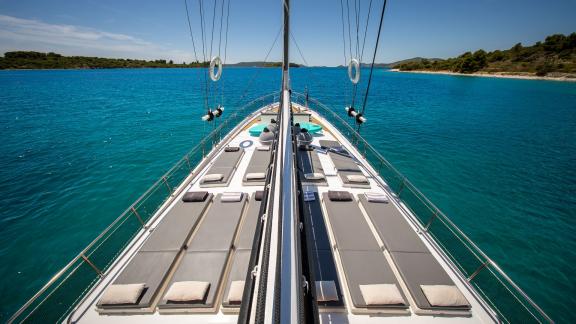 Auf dem Bugdeck der Gulet Andeo in einer türkisfarbenen Bucht stehen Reihen bequemer Liegen.