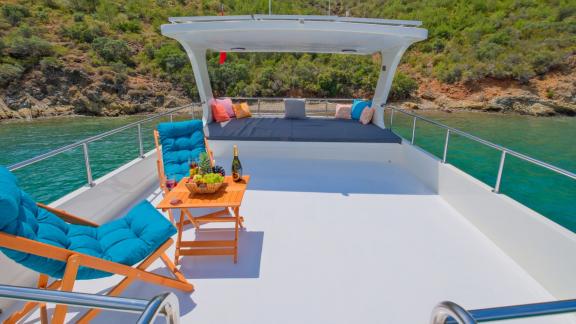 Upper deck of Gulet Anes with comfortable seating and a table, perfect for relaxing in a tranquil bay.