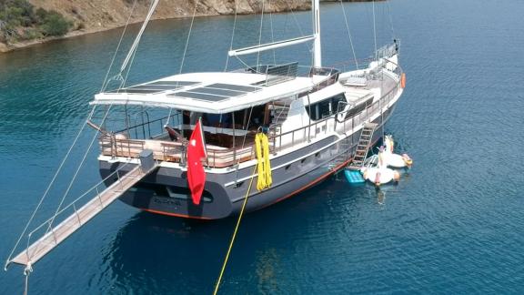 Die Gulet Arni liegt in ruhigem Wasser vor Anker, mit einer türkischen Flagge und aufblasbaren Spielzeugen.