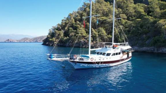 Die Gulet Avuncan liegt vor einer grünen Küste in der Ägäis vor Anker, umgeben von klarem, blauem Wasser.