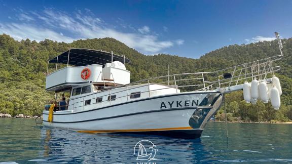 Gulet Ayken is anchored in a peaceful bay surrounded by green hills.