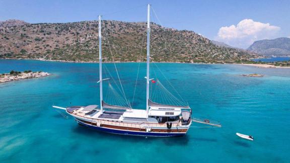 An elegant gulet with two masts anchors in a turquoise-coloured bay surrounded by picturesque hills near Marmaris.