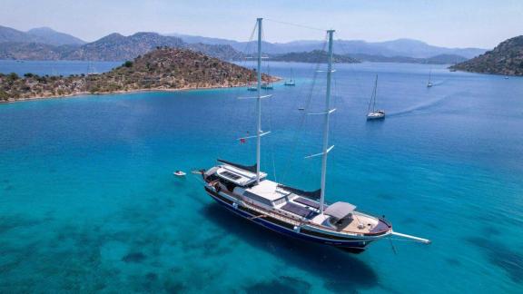 A luxurious gulet is moored in a quiet, turquoise-coloured bay near Marmaris, surrounded by rolling hills and other sail