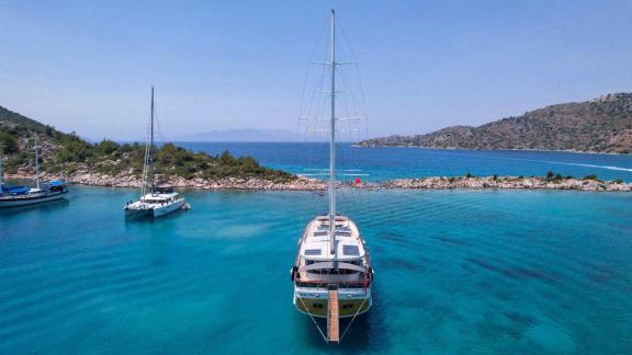 An elegant gulet anchors in an idyllic, turquoise-coloured bay near Marmaris, surrounded by rolling hills and other sail