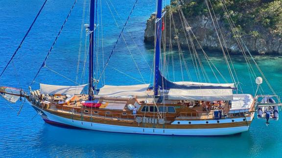 The gulet Barka is peacefully anchored in a tranquil cove, surrounded by blue waters.