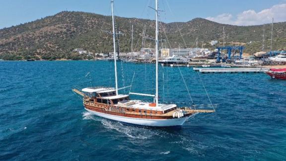 Гулет Be Happy плывет по голубым водам Бодрума с видом на гавань и холмы.