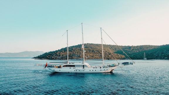 The elegant gulet Bella Mare sails in the calm waters of Bodrum, framed by an impressive rocky landscape.