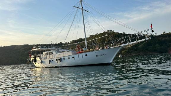 Die stilvolle Gulet Bohemian liegt vor Anker im ruhigen, türkisblauen Wasser, umgeben von üppiger Küstenlandschaft.