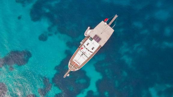 The Gulet Cagan 2 floats over crystal-clear turquoise waters, captured in a stunning aerial shot.