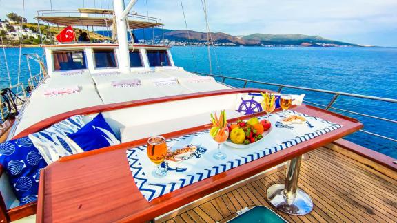 A richly set breakfast table on the deck of Gulet Cagan 2 with fresh fruit and drinks, surrounded by calm sea and coasta