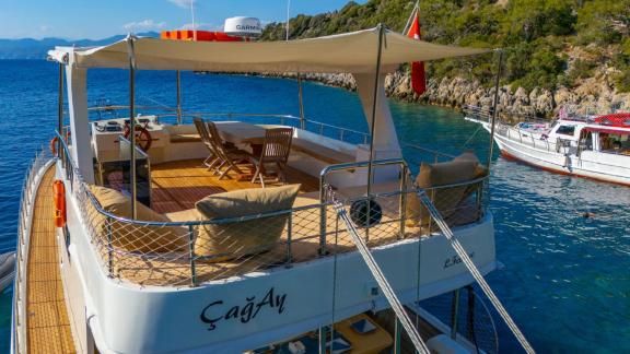 The upper deck of Gulet ÇağAy offers a comfortable lounge area with seating and sunshade in a tranquil bay.