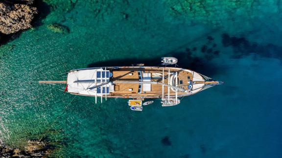 The gulet Caner 4 from above, anchored in clear, turquoise-coloured water, surrounded by rocks and nature.