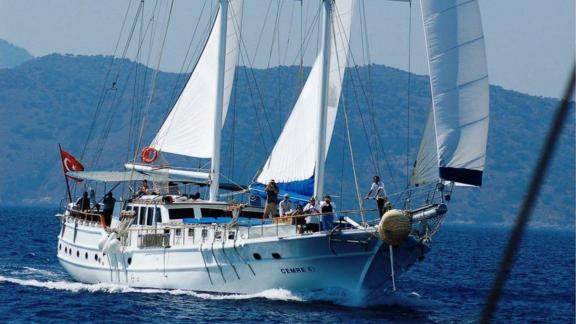 Gulet Cemre 4 sailing with sails up against a backdrop of mountains.