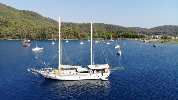 Gulet Cemre 4 is anchored in the blue sea against green hills.