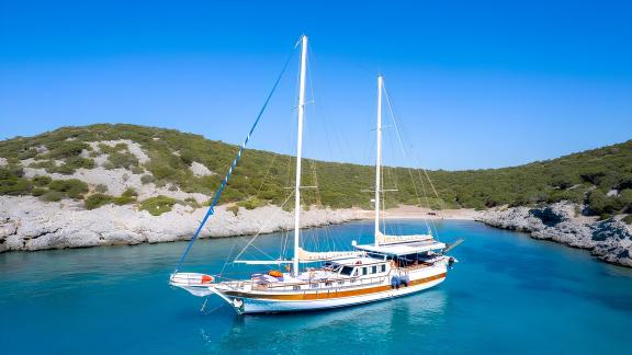 Die Gulet Cemre Junior ankert in einer ruhigen Bucht, umgeben von grüner Natur und blauem Meer.